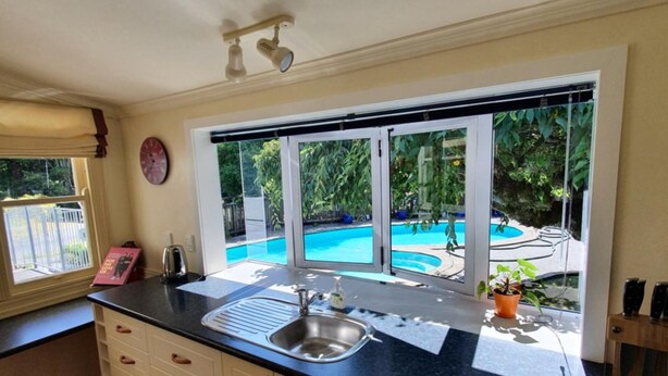 A kitchen with a large window overlooking a swimming pool. - Poripori Homestead (Lower Kaimai)