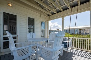 Eine überdachte Veranda mit weißen Stühlen und einem Tisch, einer Schaukel und Blick auf ein Haus im Hintergrund.