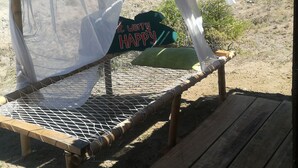 A wooden bench with a mosquito net overhead, a green sign with "Don't worry, be HAPPY" text, and a view of a dry, hilly landscape. - Qji Bio Hotel Glamping (Villavieja)