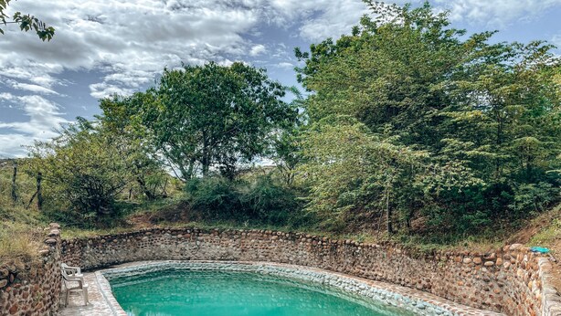 A stone pool surrounded by a stone wall, with trees and a cloudy sky in the background. - Qji Bio Hotel Glamping (Villavieja)