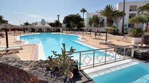 Une piscine entourée de bâtiments, agrémentée de chaises longues et de palmiers.