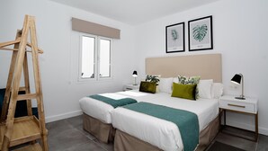 Une chambre à coucher avec un lit, des tables de chevet, une échelle en bois, une fenêtre et deux reproductions botaniques encadrées accrochées au mur.
