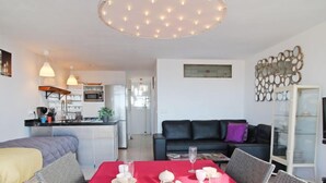 A modern living room with a dining table set for a meal, a black leather sofa, and a kitchen in the background. - Park Playa Levante by Interhome (Benidorm)