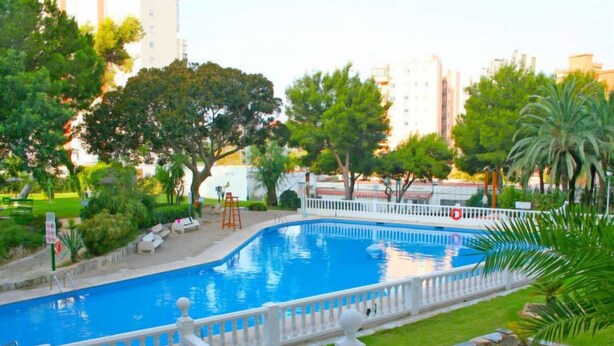 A swimming pool with a white fence and a grassy area with trees. - Park Playa Levante by Interhome (Benidorm)