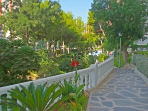 A stone pathway with a white balustrade, surrounded by lush greenery and trees.