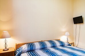 Une chambre d’hôtel avec un lit, deux lampes de chevet, un téléviseur fixé au mur et une table de chevet en bois.