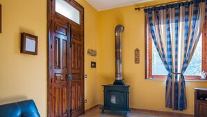 Une pièce avec une porte en bois, un poêle noir, un canapé bleu et une fenêtre ornée de rideaux à rayures.