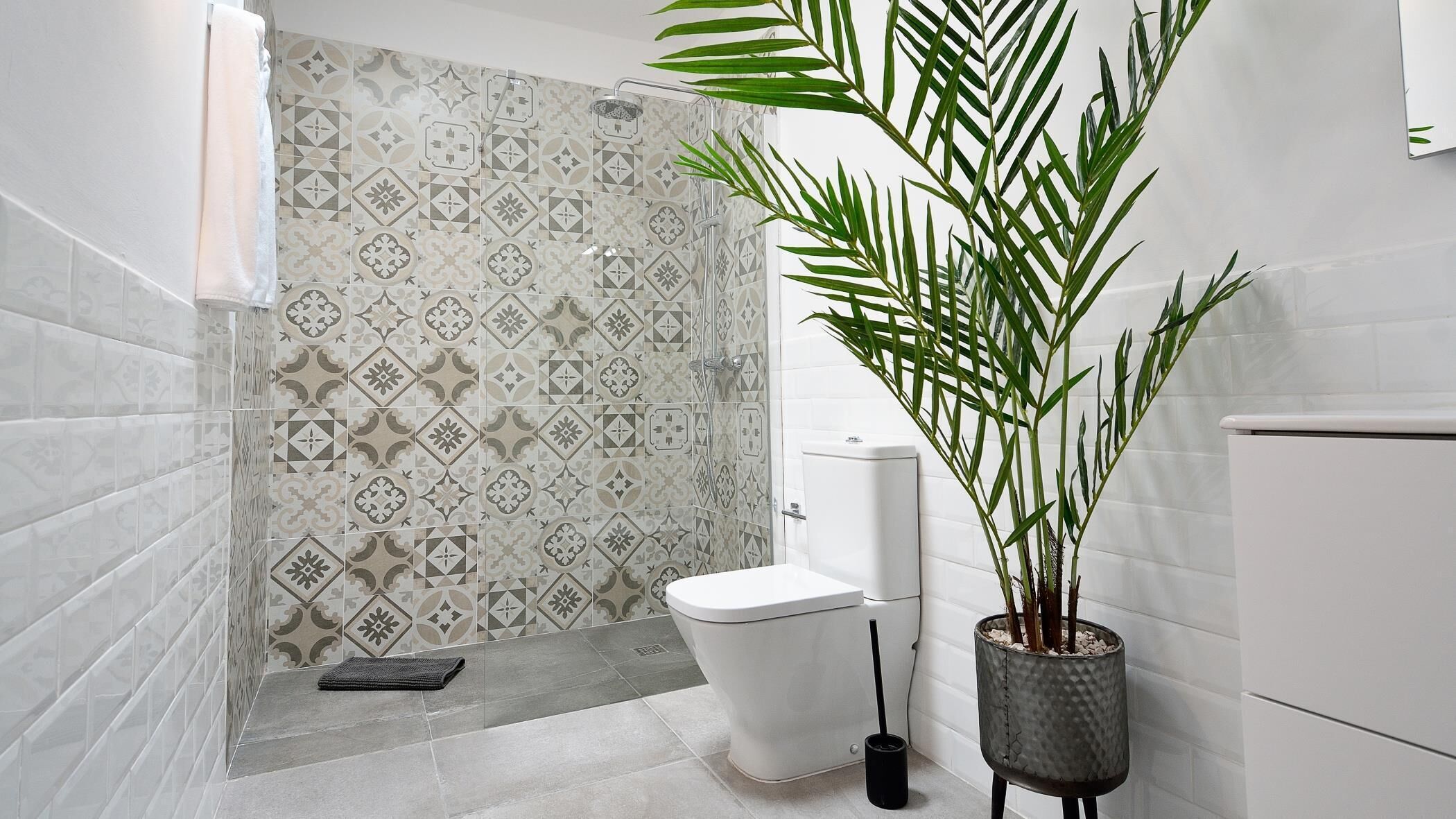 A bathroom with patterned tiles, a toilet, a shower, and a potted plant.