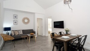 A modern living room with a sofa, coffee table, and dining area with chairs and a TV. - Suite Costa Kenia close to Playa Bastian with Pool By PVL (Costa Teguise)