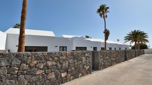 A modern building with white exterior walls, a stone wall in front, and palm trees. - Suite Costa Kenia close to Playa Bastian with Pool By PVL (Costa Teguise)