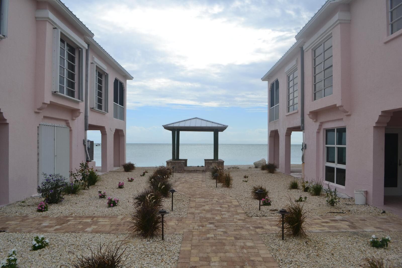A building with a paved pathway leading to a gazebo overlooking the sea.