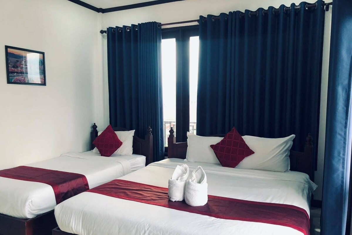 Habitación de hotel con dos camas, cortinas oscuras, ropa de cama blanca y un par de toallas blancas sobre la cama.