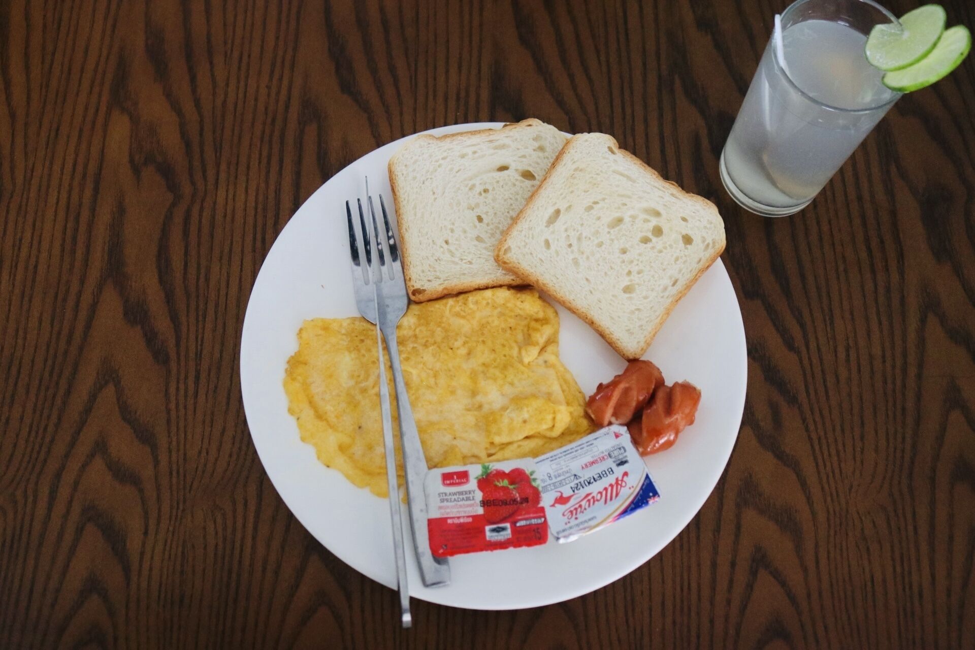 A plate with scrambled eggs, bacon, and toast on a wooden table.
