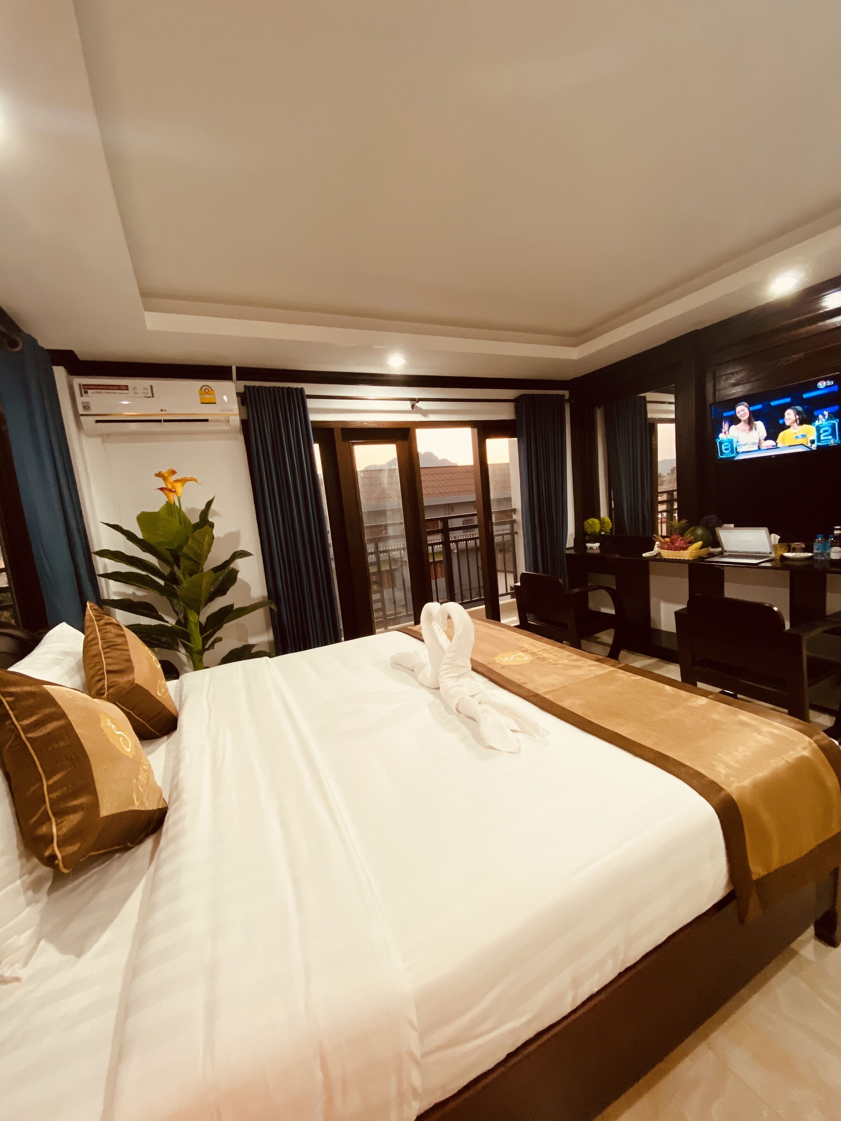A hotel room with a large bed, a desk, a television, and a balcony with a view.