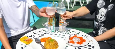 Una mesa redonda con mantel blanco y negro estampado, dos platos de comida y dos latas de cerveza.