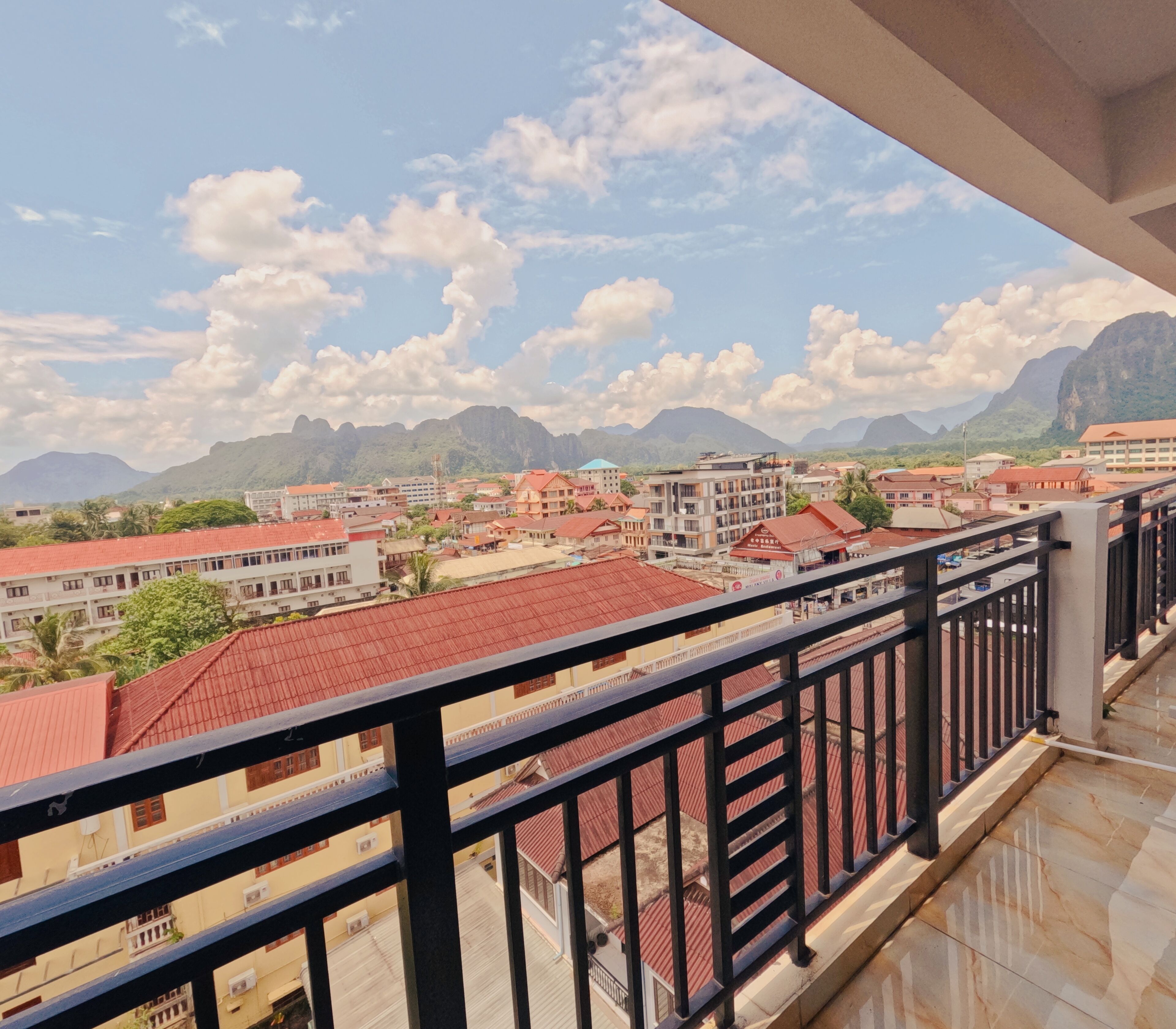 A balcony with a view of a town with red-roofed buildings and mountains in the background.