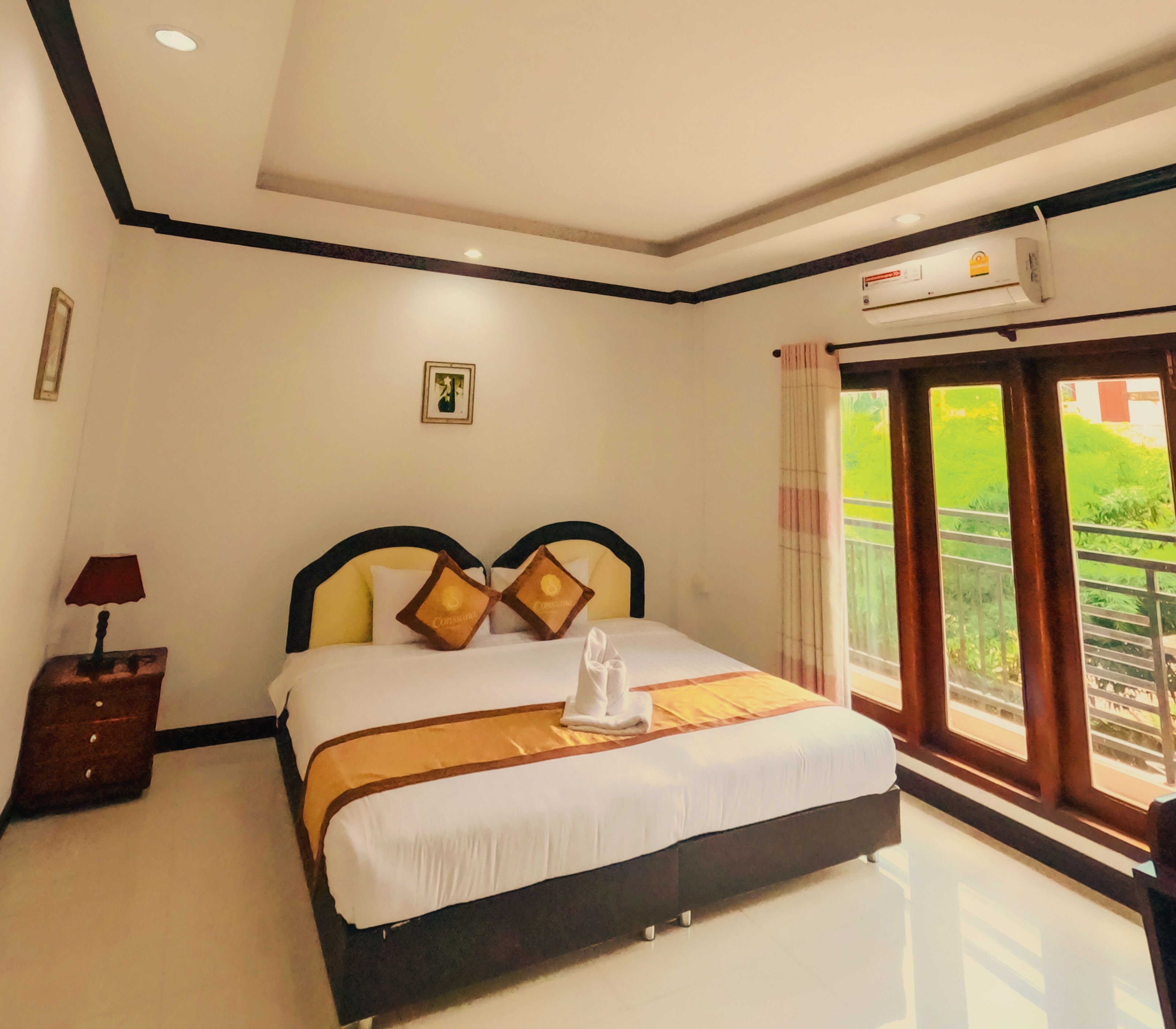 A hotel room with a bed, a nightstand, a picture on the wall, and a window with a view of greenery.