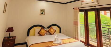A hotel room with a bed, a nightstand, a picture on the wall, and a window with a view of greenery.