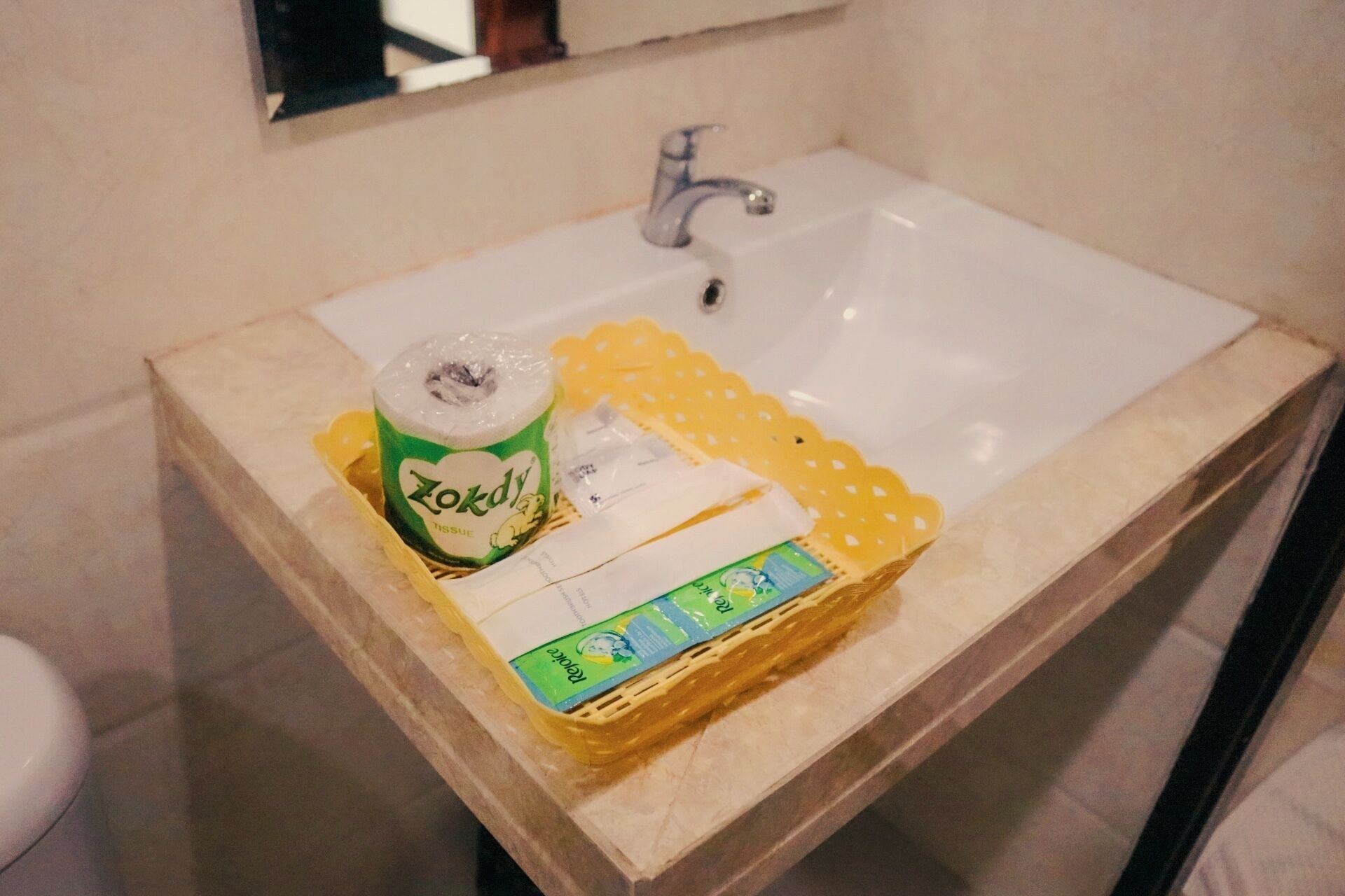 A bathroom sink with a white basin, a green and white toilet paper roll, a yellow tissue holder, and a measuring tape.