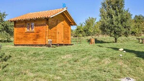 A wooden cabin with a tiled roof, a small porch, and a grassy yard. - Holiday home mit Terrasse und Klimaanlage (Petehi)