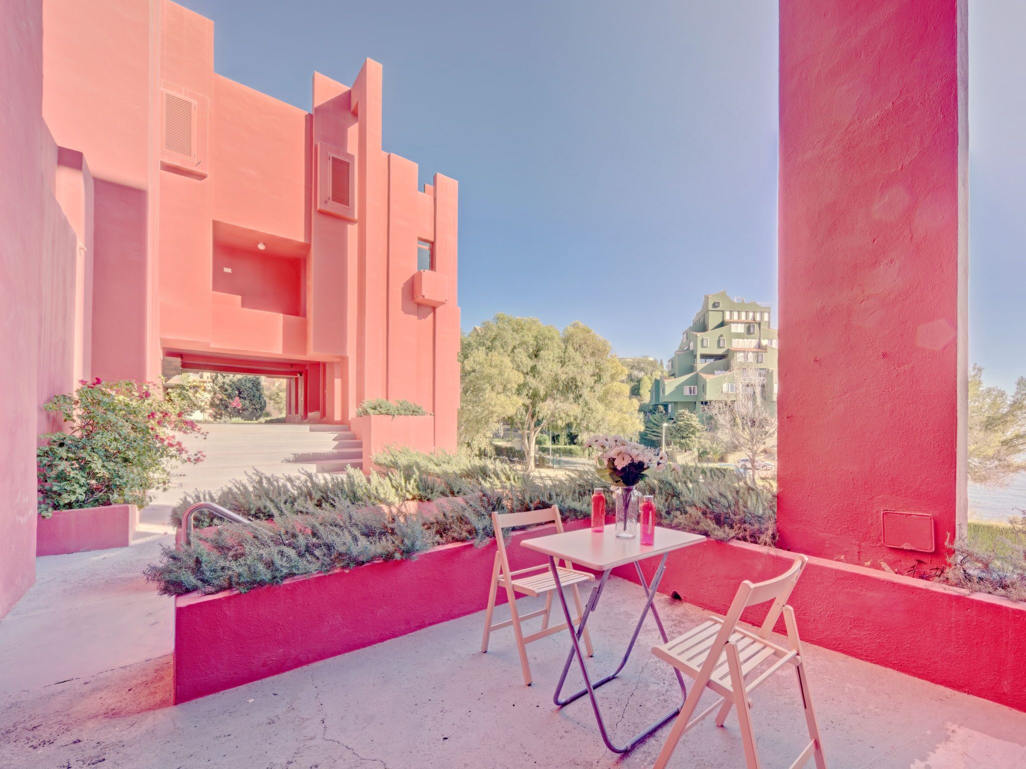 Edifício moderno com paredes cor-de-rosa e um pátio com mesa e cadeiras.