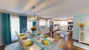 Una cocina moderna con armarios blancos, un refrigerador de acero inoxidable y un comedor con una mesa lista para cuatro.
