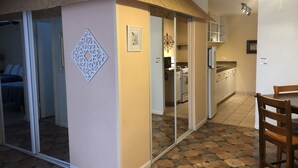 Ein Zimmer mit einer Schiebetür zu einem Schlafzimmer, eine Küche mit weißen Geräten und ein Essbereich mit einem Holztisch und Stühlen.