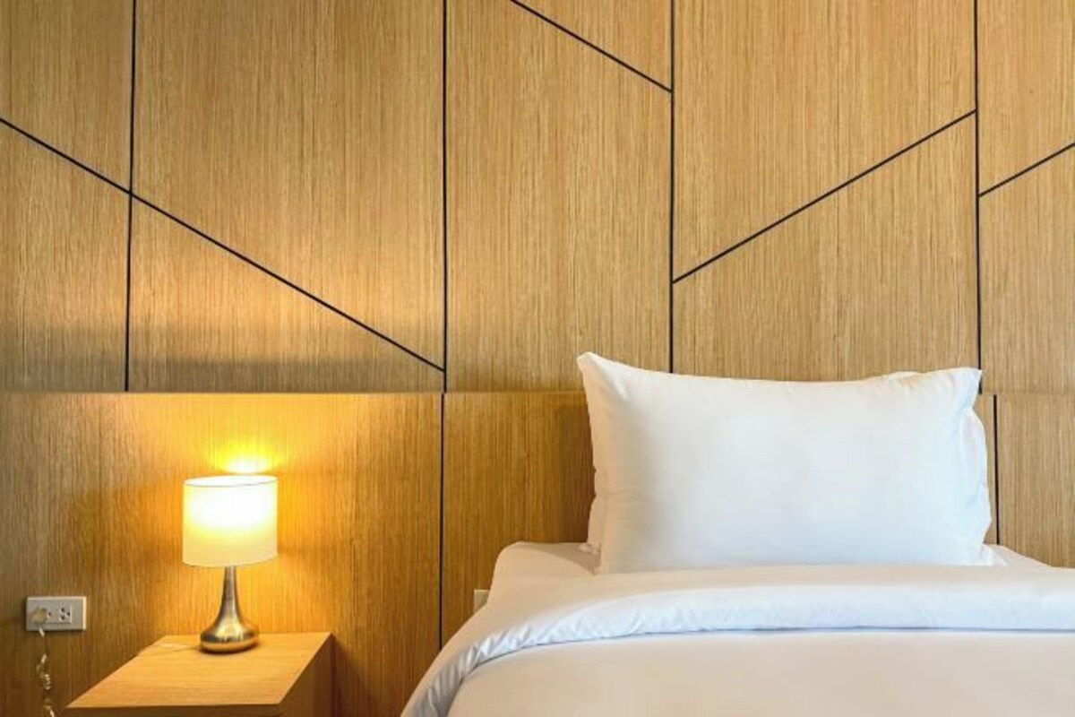 Una habitación de hotel con una cama, una lámpara de noche y un panel de pared de madera.