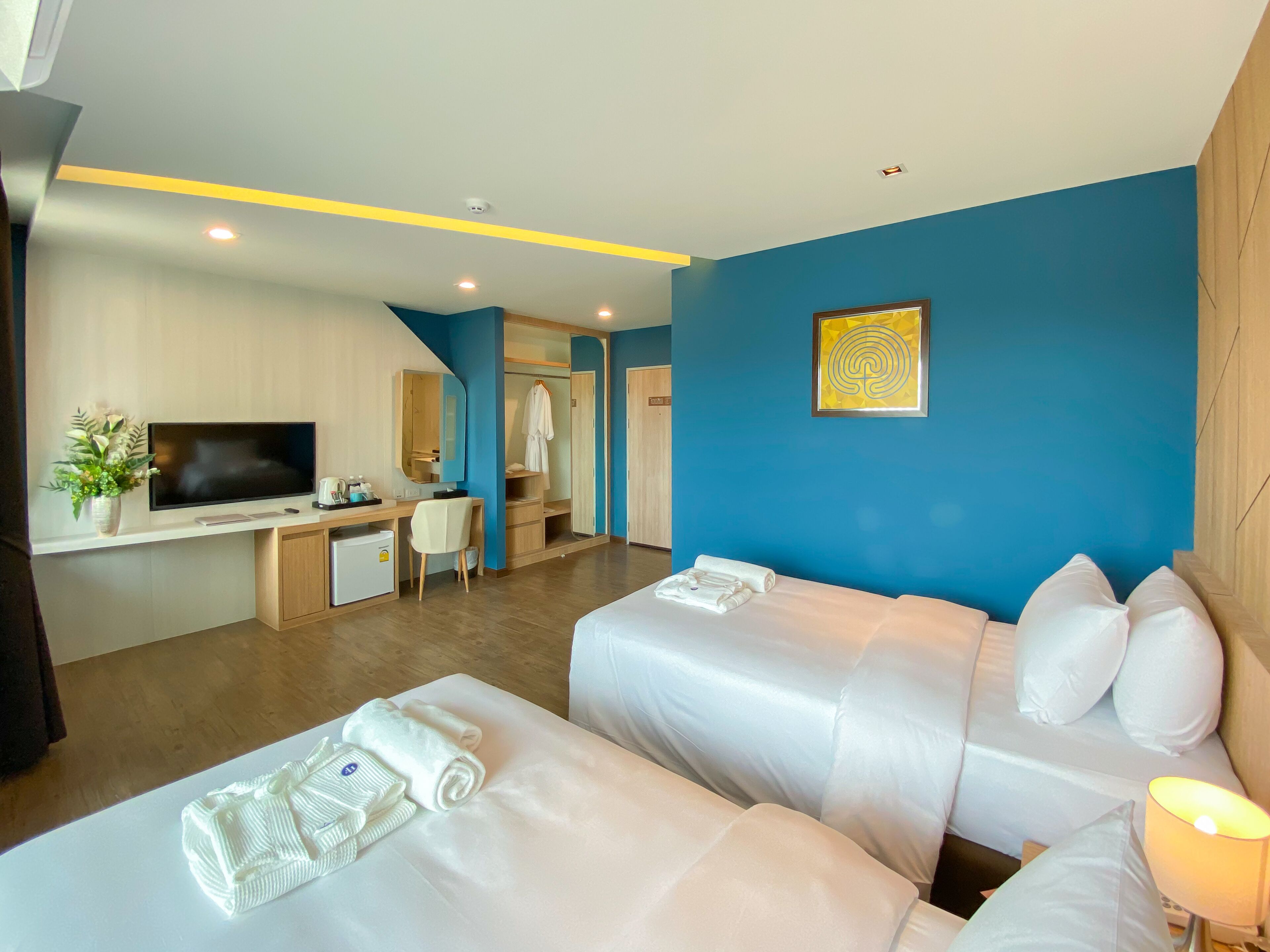 A hotel room with two beds, a desk with a TV, a small fridge, and a bathroom visible through an open door.