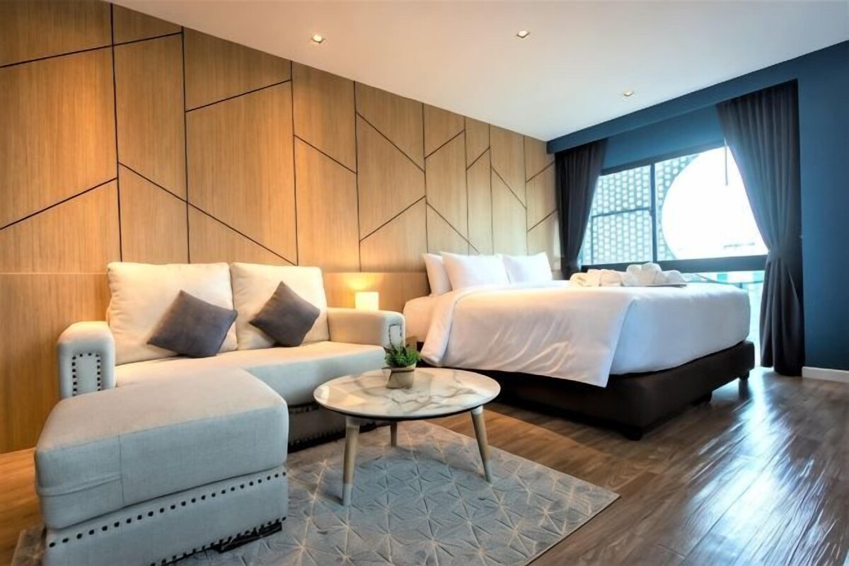 Una habitación de hotel moderna con sofá, cama, una mesita redonda y un ventanal grande.