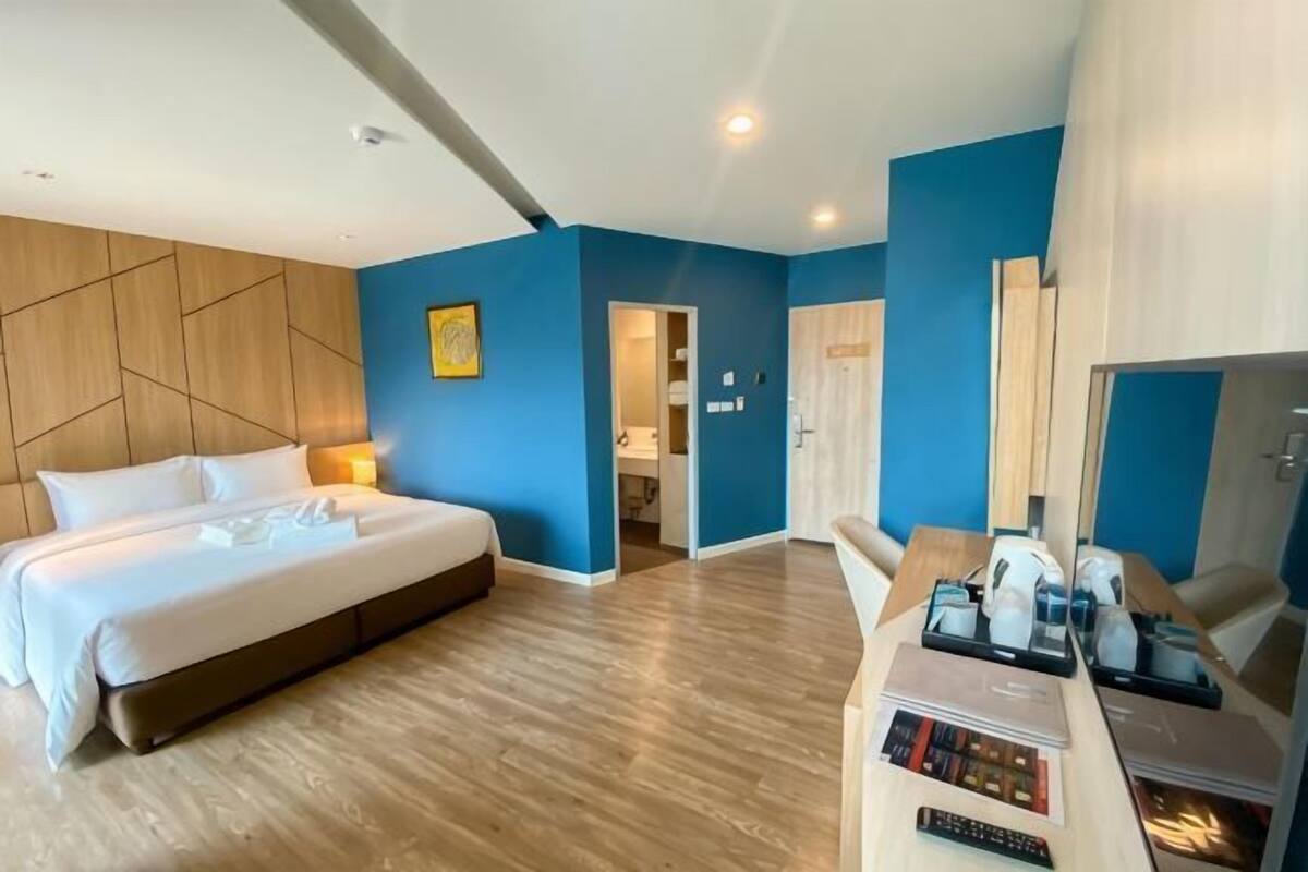 A hotel room with a large bed, a desk with a computer, and a door leading to a bathroom.