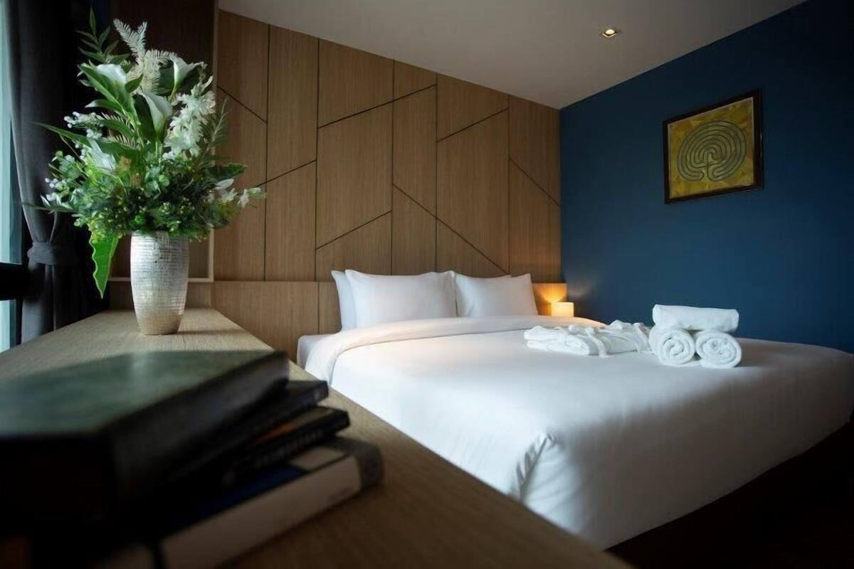 A hotel room with a large bed, a bedside table with a vase of flowers, and a wall with a geometric pattern.