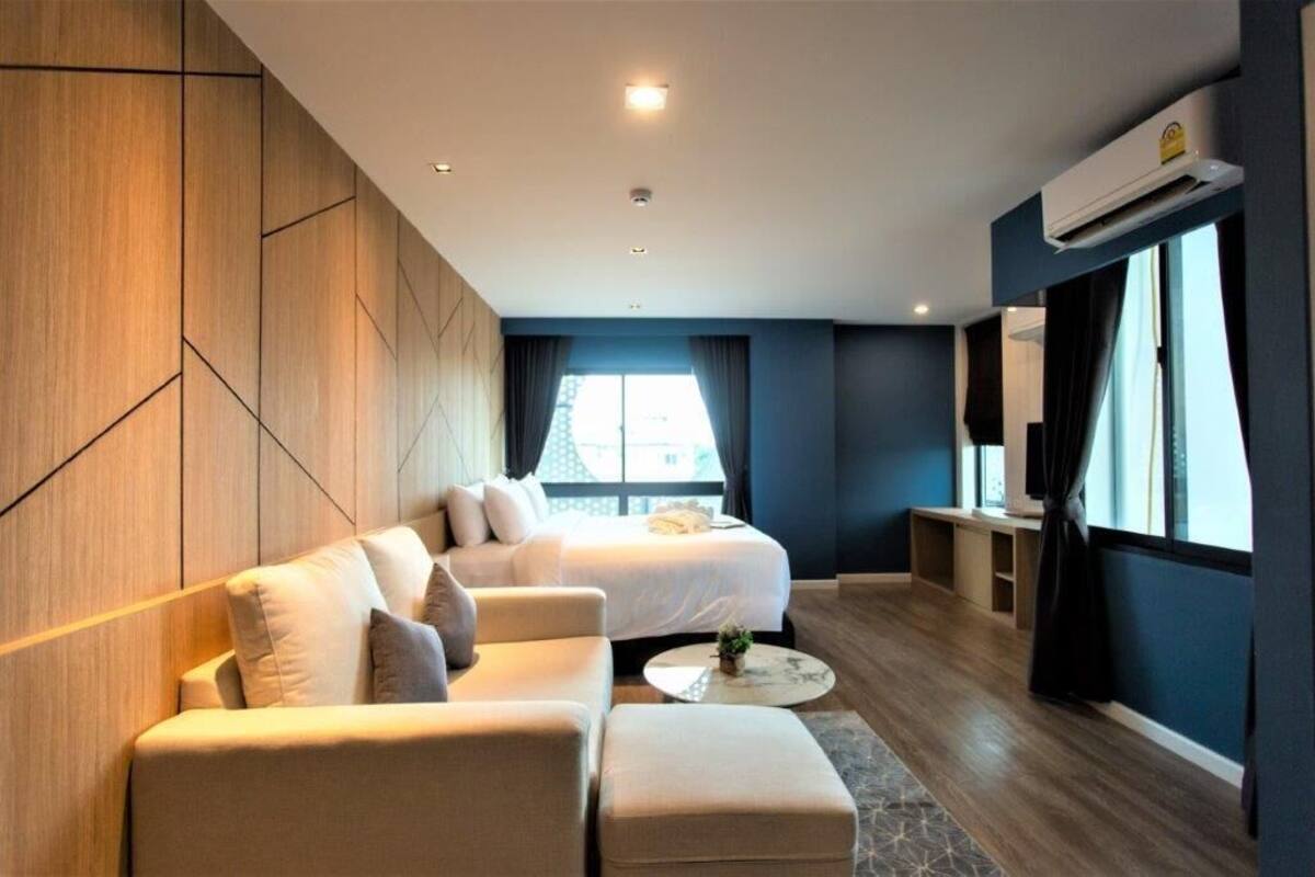 A modern hotel room with a bed, two sofas, a coffee table, and a TV.