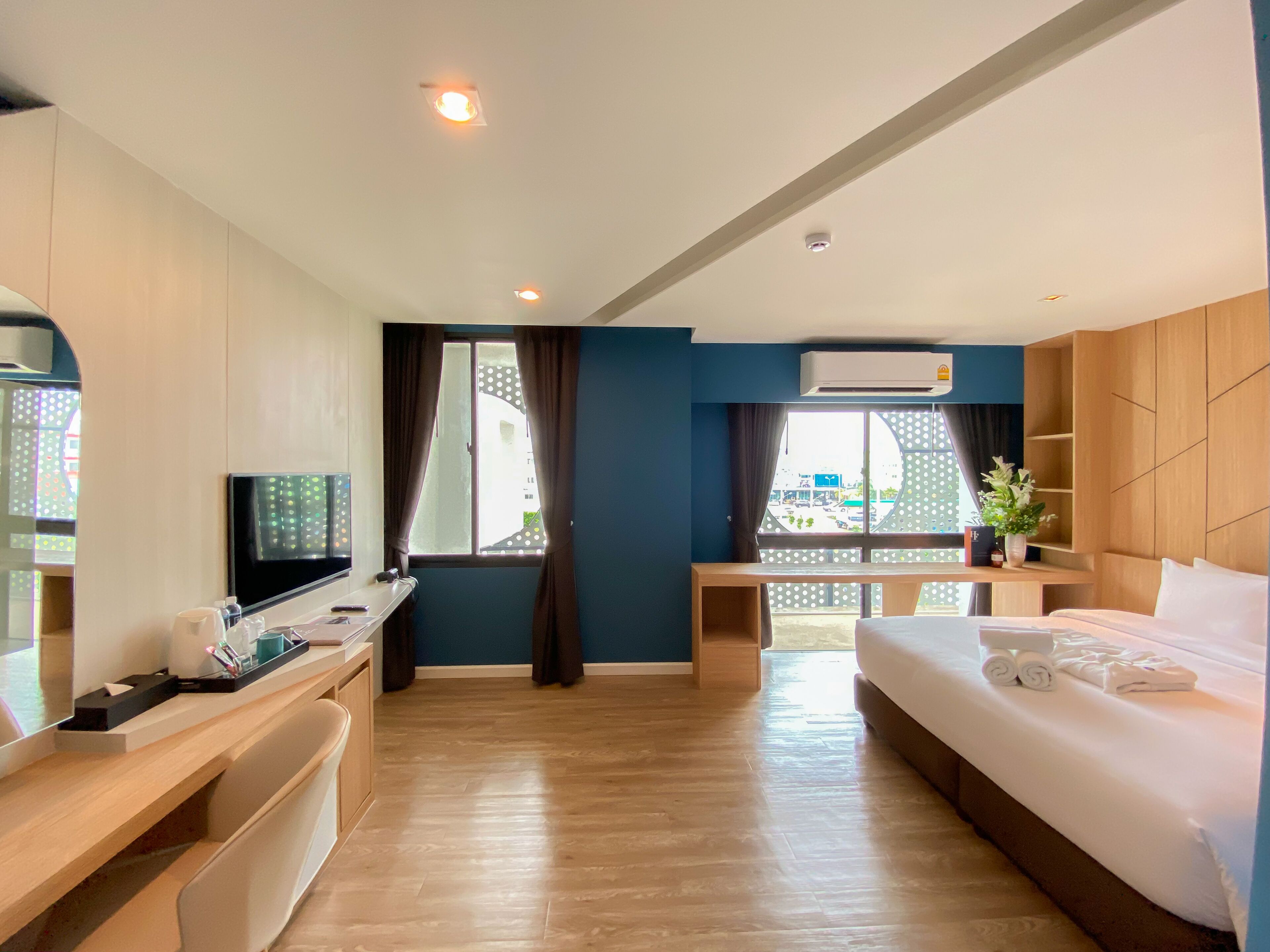 A hotel room with a bed, a desk with a TV, a window with curtains, and a view of the outside.