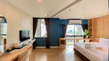A hotel room with a bed, a desk with a TV, a window with curtains, and a view of the outside.