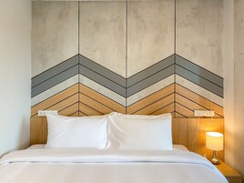Cama com roupa de cama branca, cabeceira de madeira e parede com padrão geométrico.