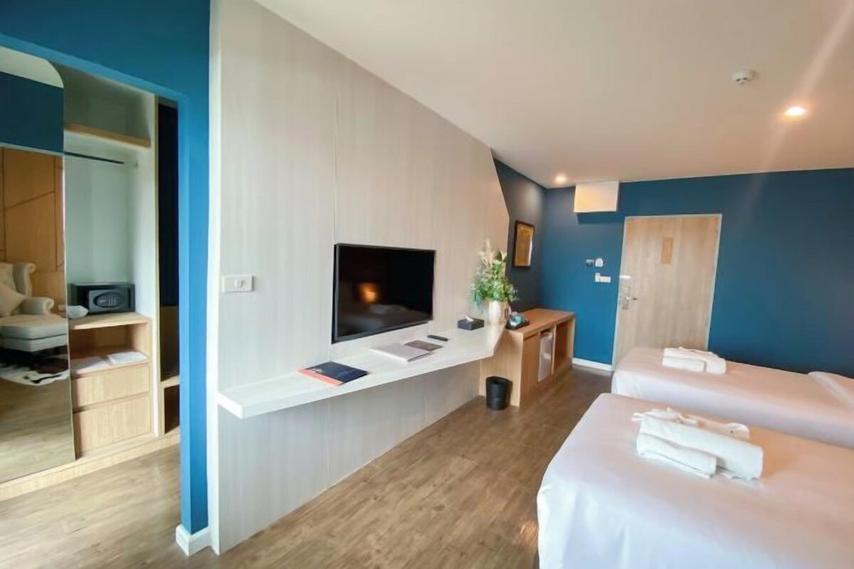 Habitación de hotel con televisión, mesitas de noche, un espejo, armario y dos camas.