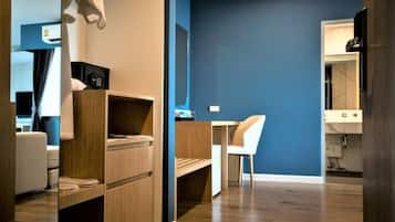 Una habitación de hotel moderna con un escritorio de madera, una silla, un estante pequeño y una pared de acento azul.
