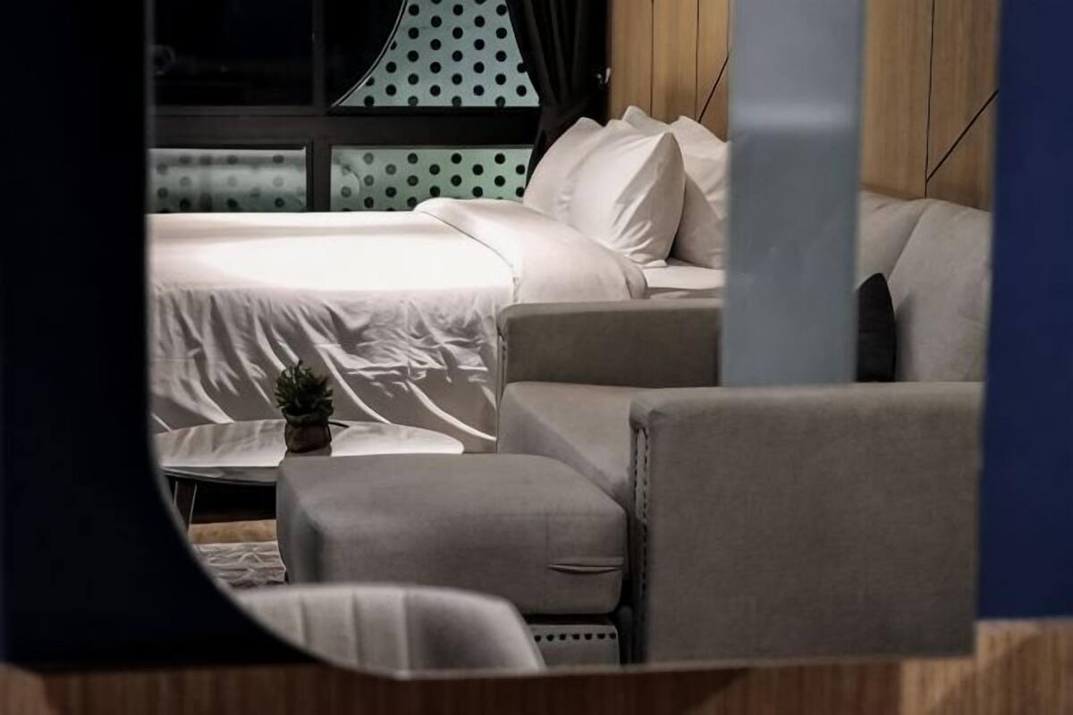 A bedroom with a bed, a sofa, a small table, and a potted plant.