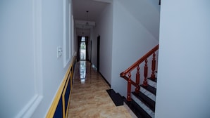 A hallway with a marble floor, a wooden staircase with red balusters, and a ceiling light fixture. - Rome Hostel (Tuy Hoa)
