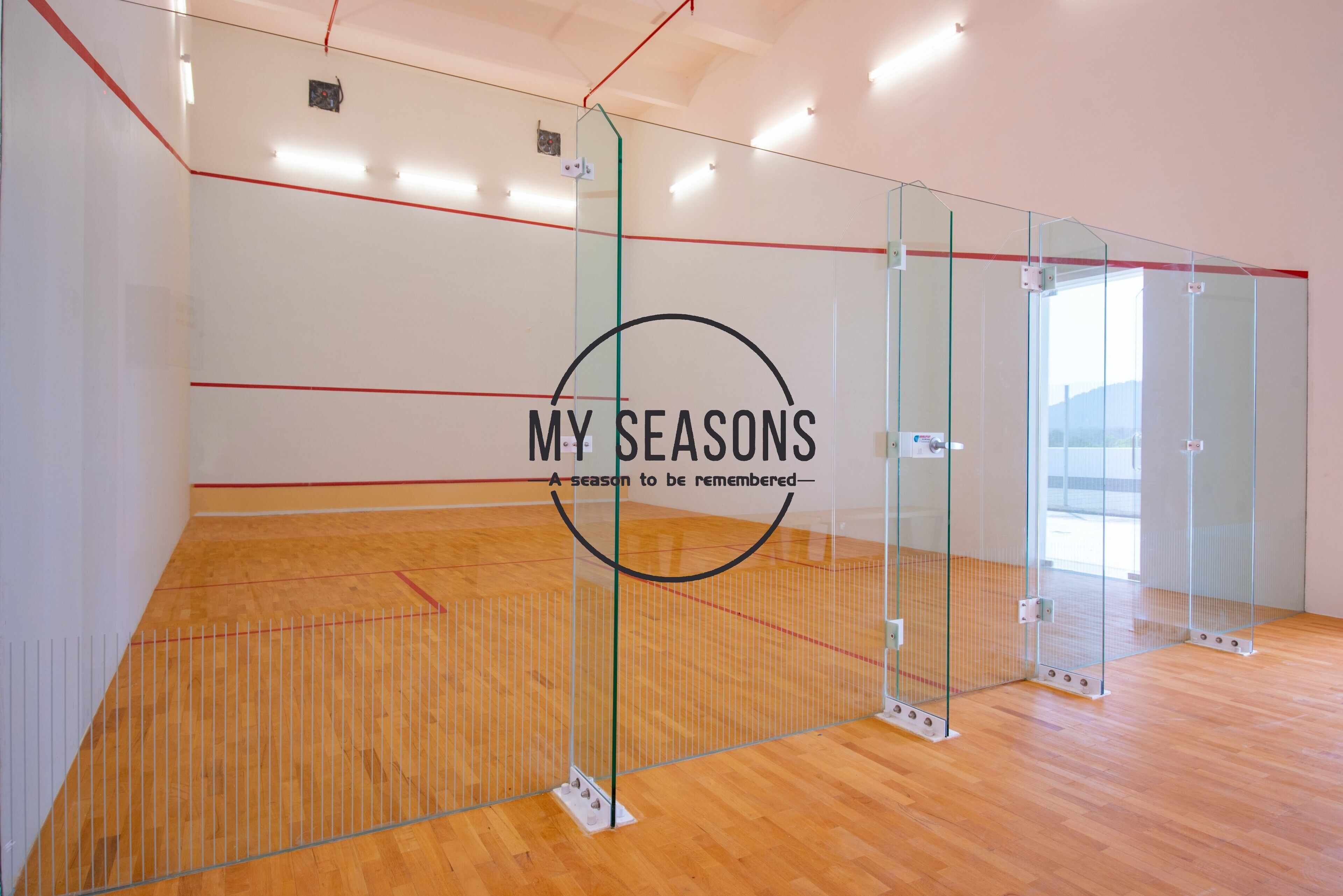 Una cancha de squash con paredes de vidrio y suelo de madera.