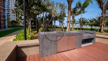 Een aangelegde tuin met een stenen bankje, palmbomen en uitzicht op een hoog gebouw.