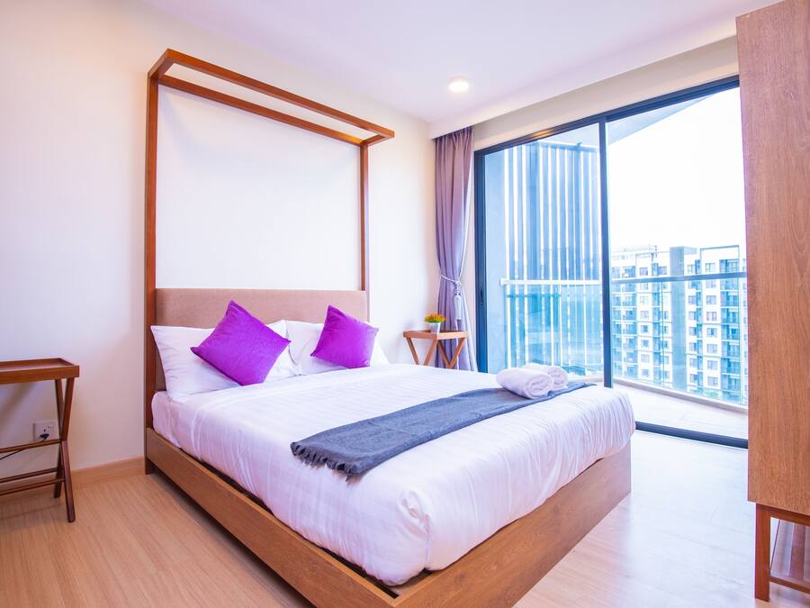 Ein modernes Hotelzimmer mit einem großen Bett, einem Holz-Kopfteil und Blick auf die Stadt durch raumhohe Fenster.
