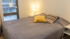 A bedroom with a bed, a bedside lamp, and a window with blinds.