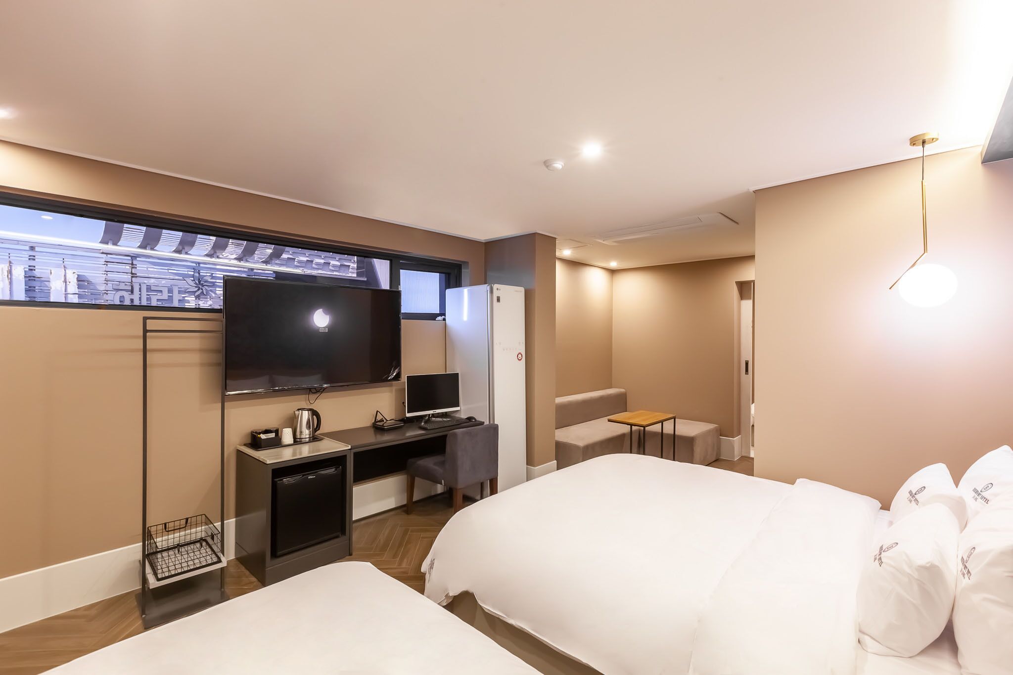 Habitación de hotel con cama, escritorio con computadora, televisor y ventana con vista a la ciudad.
