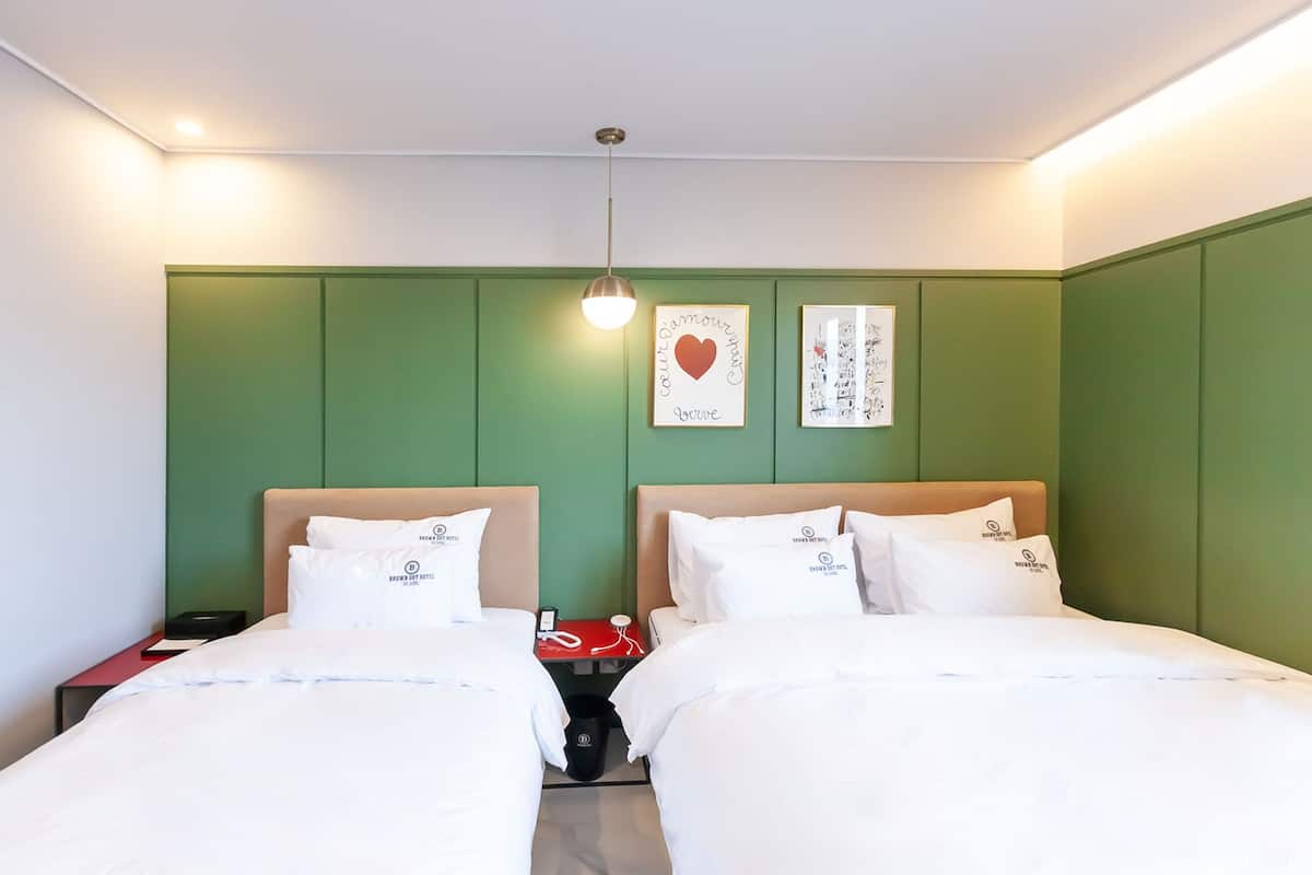 Ein Hotelzimmer mit zwei Betten, grünen Wänden, einer Pendelleuchte und zwei gerahmten Bildern an der Wand.