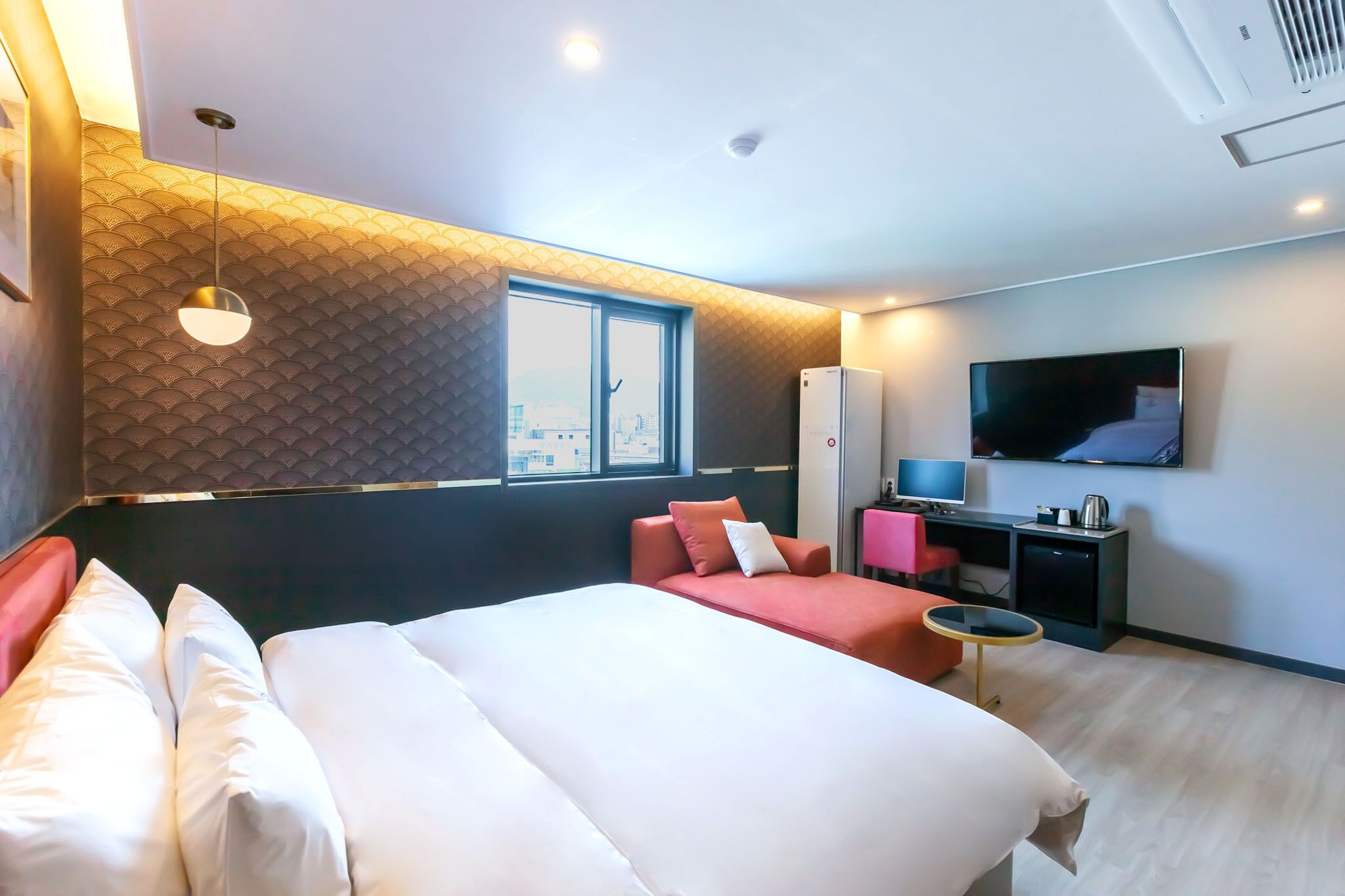 A modern hotel room with a large bed, a desk, a TV, and a window with a city view.