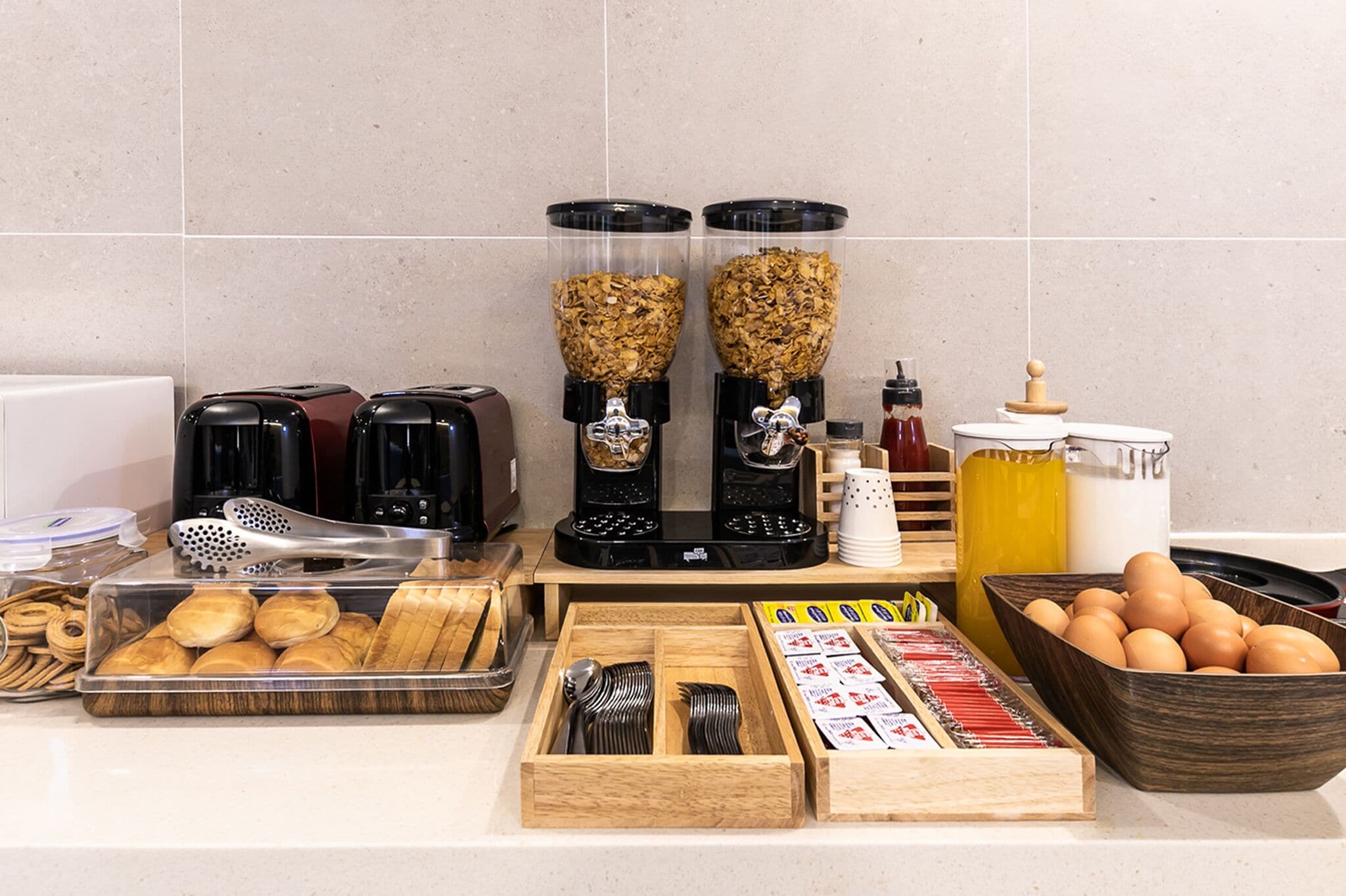 A kitchen counter with coffee makers, a toaster, a coffee grinder, a tray of pastries, a bowl of eggs, and various kitchen utensils.