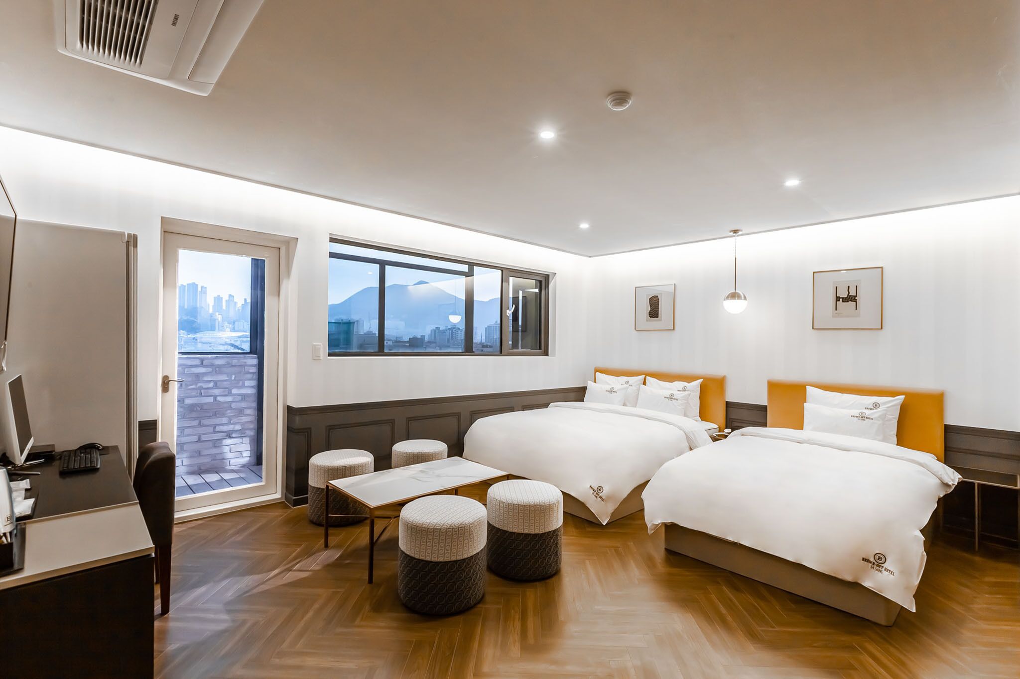 Habitación de hotel con dos camas, un escritorio, una computadora y vistas a un paisaje urbano.