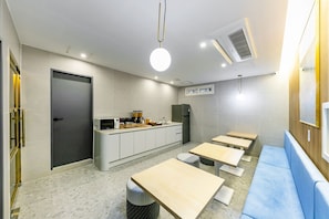 A modern kitchen with a built-in oven, microwave, and sink. There are several wooden tables and a blue bench. - Brown Dot Hotel Sasang Renecite (Busan)